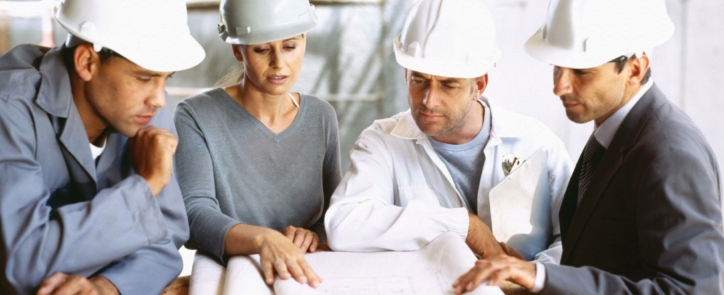 project engineer in a meeting with other project engineers standing around reading a piping and instrument diagram.